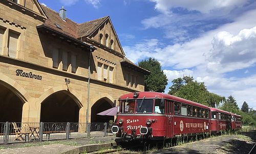 Der historische rote Schienenbus "Kloster Flitzer" hält an einem Bahnsteig vor dem Bahnhofsgebäude in Maulbronn