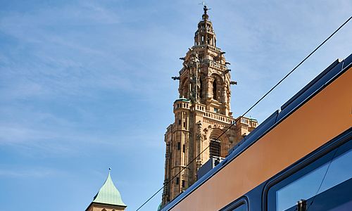 Ein fenster einer AVG-Stadtbahn. Im Hintergrund ist ein Kirchturm in der Heilbronner Innenstadt zu sehen.