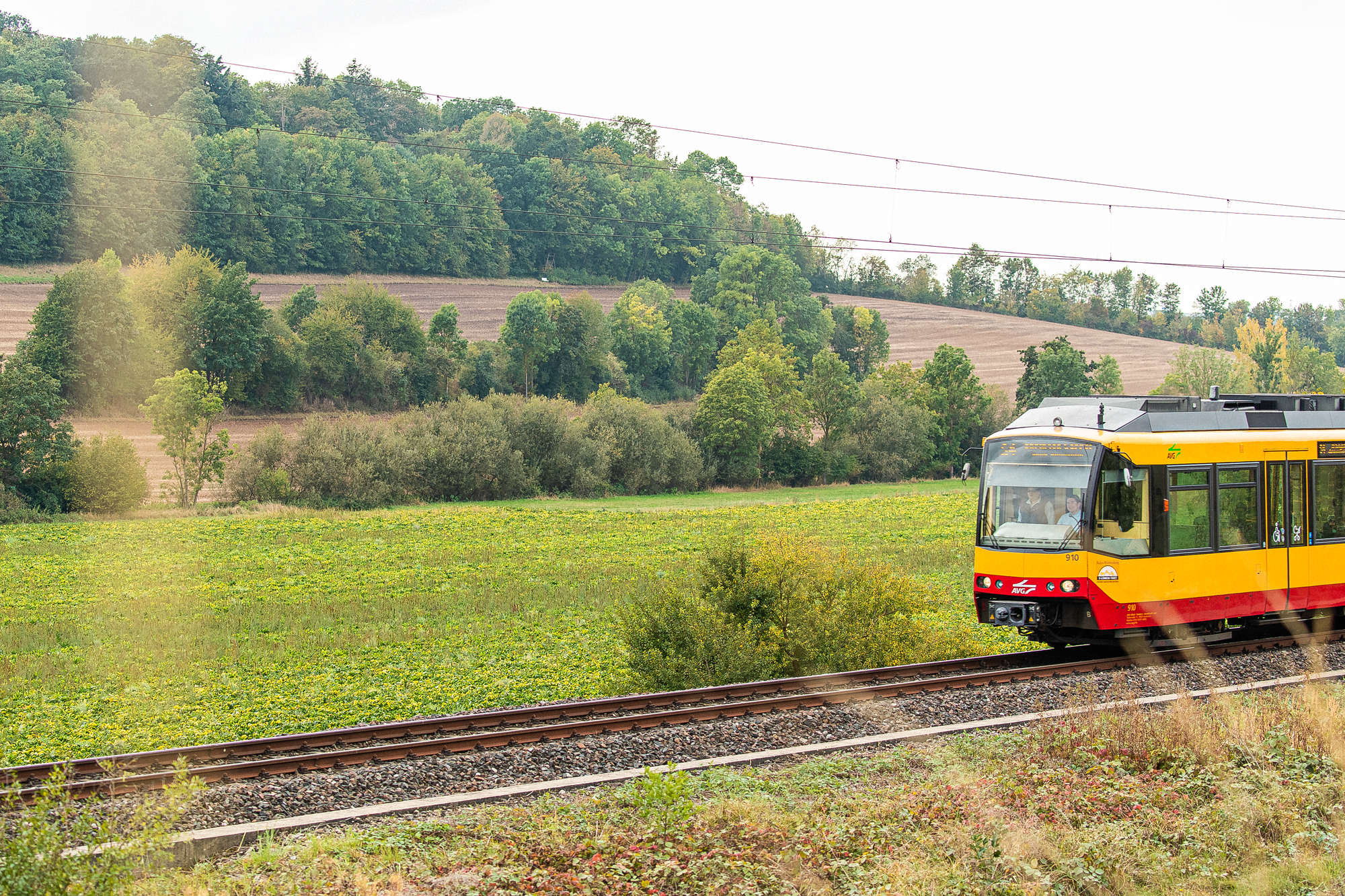 Eine AVG-Stadtbahn fährt auf der Kraichgaubahn. Im Hintergrund sind bewaldete Hügel zu sehen