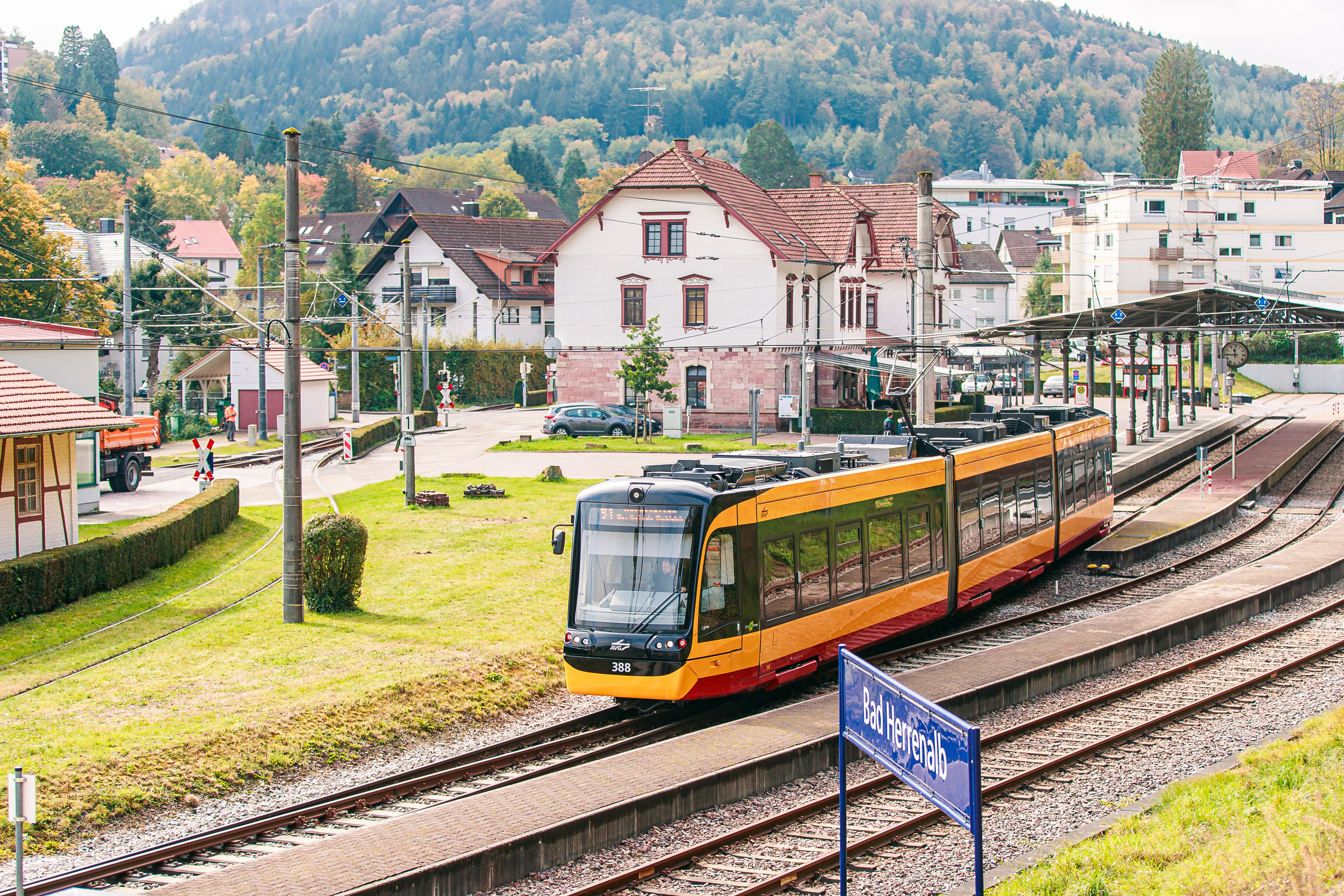 Eine AVG-Stadtbahn fährt durchs Albtal. Im Hintergrund sind Häuser und der Bahnhof Bad Herrenalb zu sehenzu sehen.